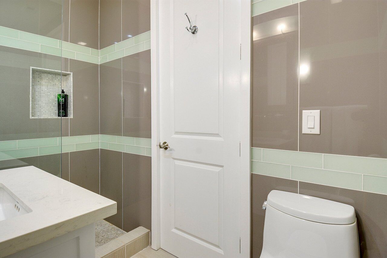 Une salle de bain avec une porte blanche, un lavabo blanc, des toilettes et un espace douche séparé par une paroi en verre.