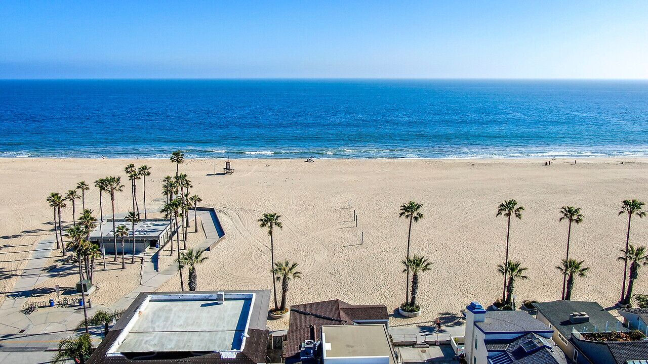Una playa con palmeras, una piscina y edificios al frente.