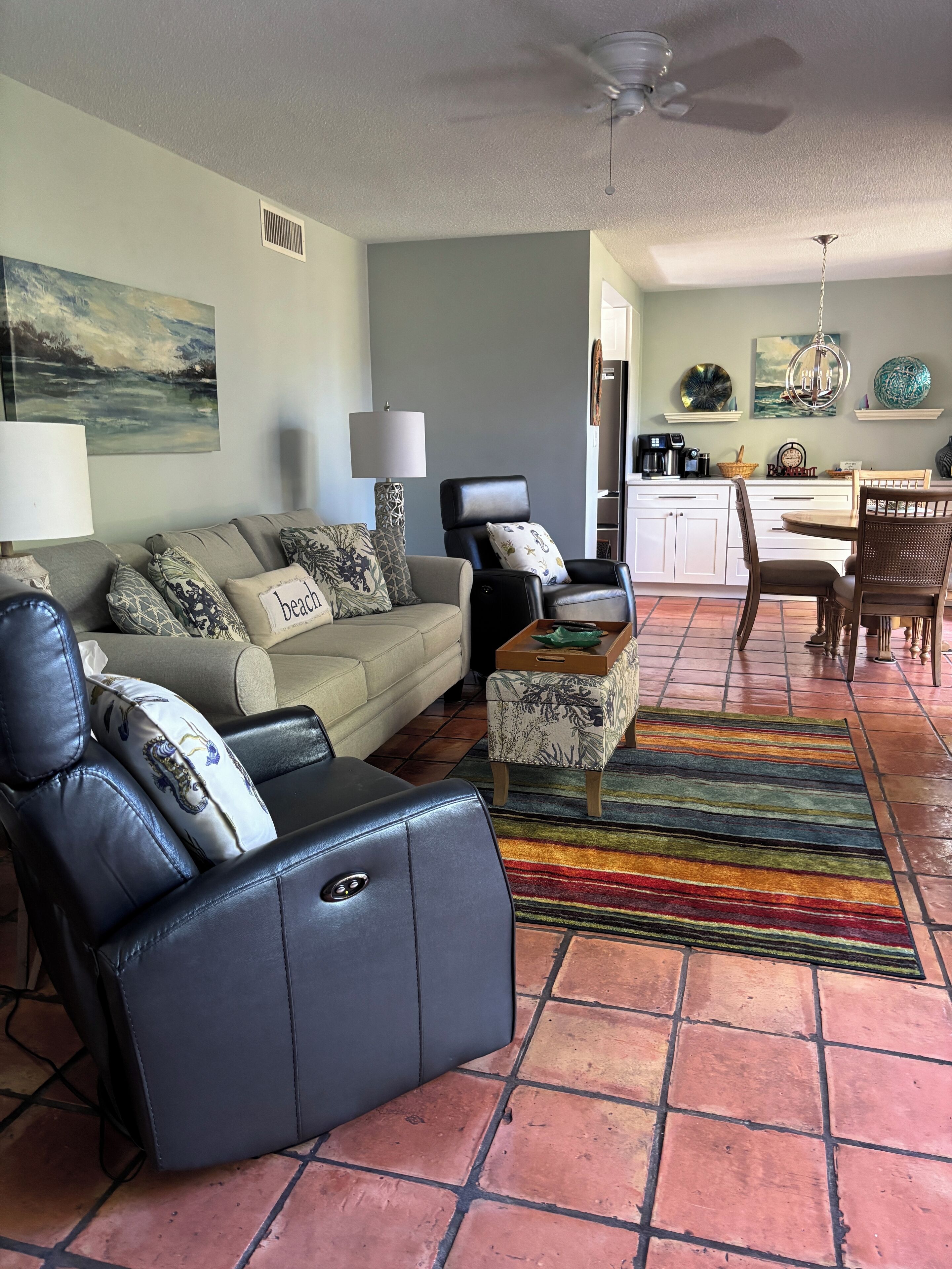 A living room with a sofa, a black leather chair, a coffee table, and a colorful rug.