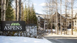 A sign for "The Aspens" with a stone wall and trees in the background. - Ski In Ski Out Great Location Hot Tub Super Clean Fully Stocked Great Reviews (Whistler)