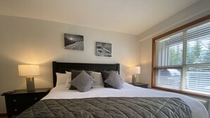 A neatly made bed with a grey quilt, two bedside lamps, and two framed pictures on the wall. - Ski In Ski Out Great Location Hot Tub Super Clean Fully Stocked Great Reviews (Whistler)