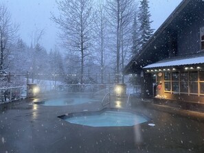 Zona exterior cubierta de nieve con piscina y un edificio iluminado.