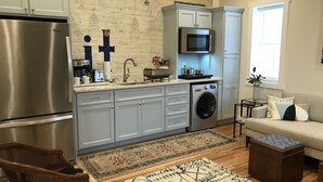 Une cuisine moderne équipée d’un réfrigérateur en acier inoxydable, d’un four encastré et d’un four à micro-ondes. Un lave-linge est intégré aux meubles de cuisine, et un coin repas comprend un canapé et une table basse.