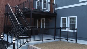 Un immeuble à la façade en briques, à l’extérieur gris et doté d’un escalier en métal noir menant à un balcon.