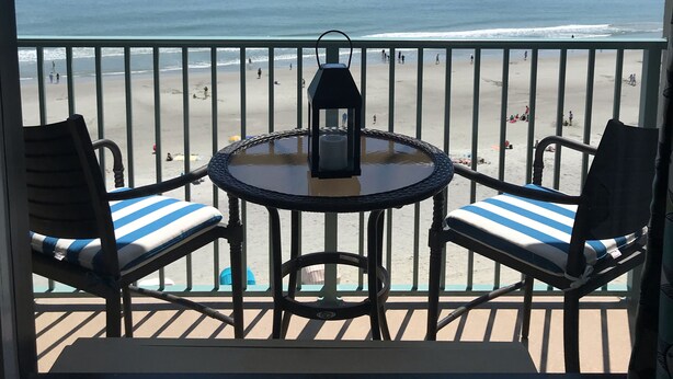 Un balcon avec vue sur la plage, deux chaises, une table et une lanterne.