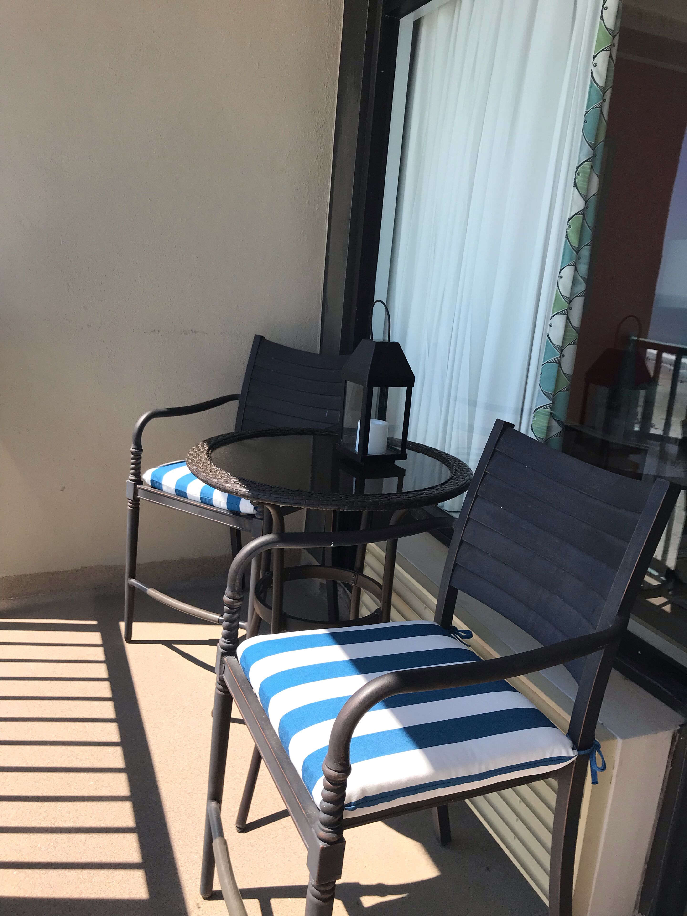 Un balcon avec une table ronde et deux chaises, dont l’une est dotée d’un coussin à rayures.