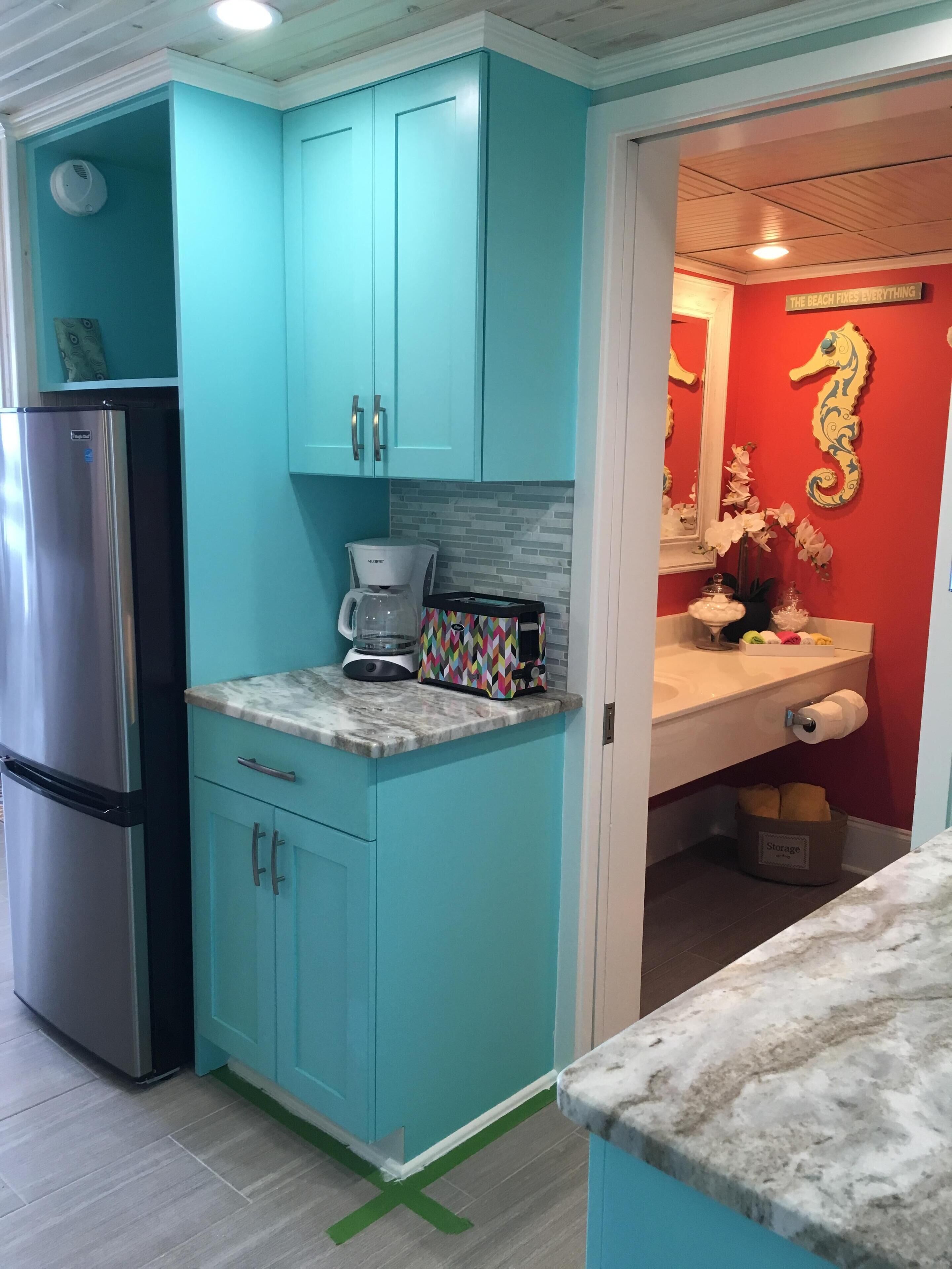 A kitchen with teal cabinets, a stainless steel refrigerator, a coffee maker, and a colorful toaster.