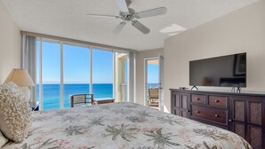 A bedroom with a large bed, a ceiling fan, a TV, and a view of the ocean. - Long Beach 2-Bedroom Condo with Two Seasonal Beach Chairs with Umbrella (Panama City Beach)