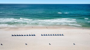 A beach with rows of blue beach chairs and a few people walking. - Long Beach 2-Bedroom Condo with Two Seasonal Beach Chairs with Umbrella (Panama City Beach)