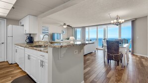 A spacious kitchen with a large island, white cabinetry, and a view of the ocean through large windows. - Long Beach 2-Bedroom Condo with Two Seasonal Beach Chairs with Umbrella (Panama City Beach)
