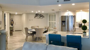Une cuisine moderne équipée d’un réfrigérateur en acier inoxydable, d’un distributeur d’eau et d’un évier. On y trouve également un coin repas avec une table et des chaises, et un ventilateur de plafond au-dessus.