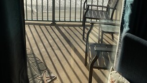 A balcony with a view of the ocean, a metal railing, and two chairs.
