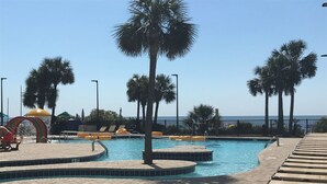 A swimming pool with a tiled deck, lounge chairs, palm trees, and a view of the ocean.