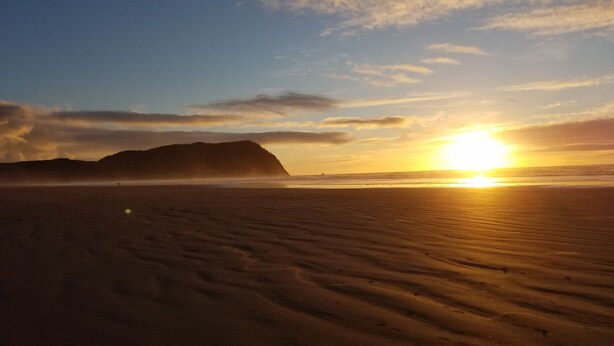 Ein Strand mit Sonnenuntergang, Dünen und einem entfernten Berg.