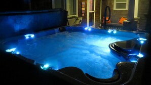 Ein Whirlpool mit blauer Beleuchtung, eine Außenwand aus Stein und eine Tür zu einer überdachten Terrasse.