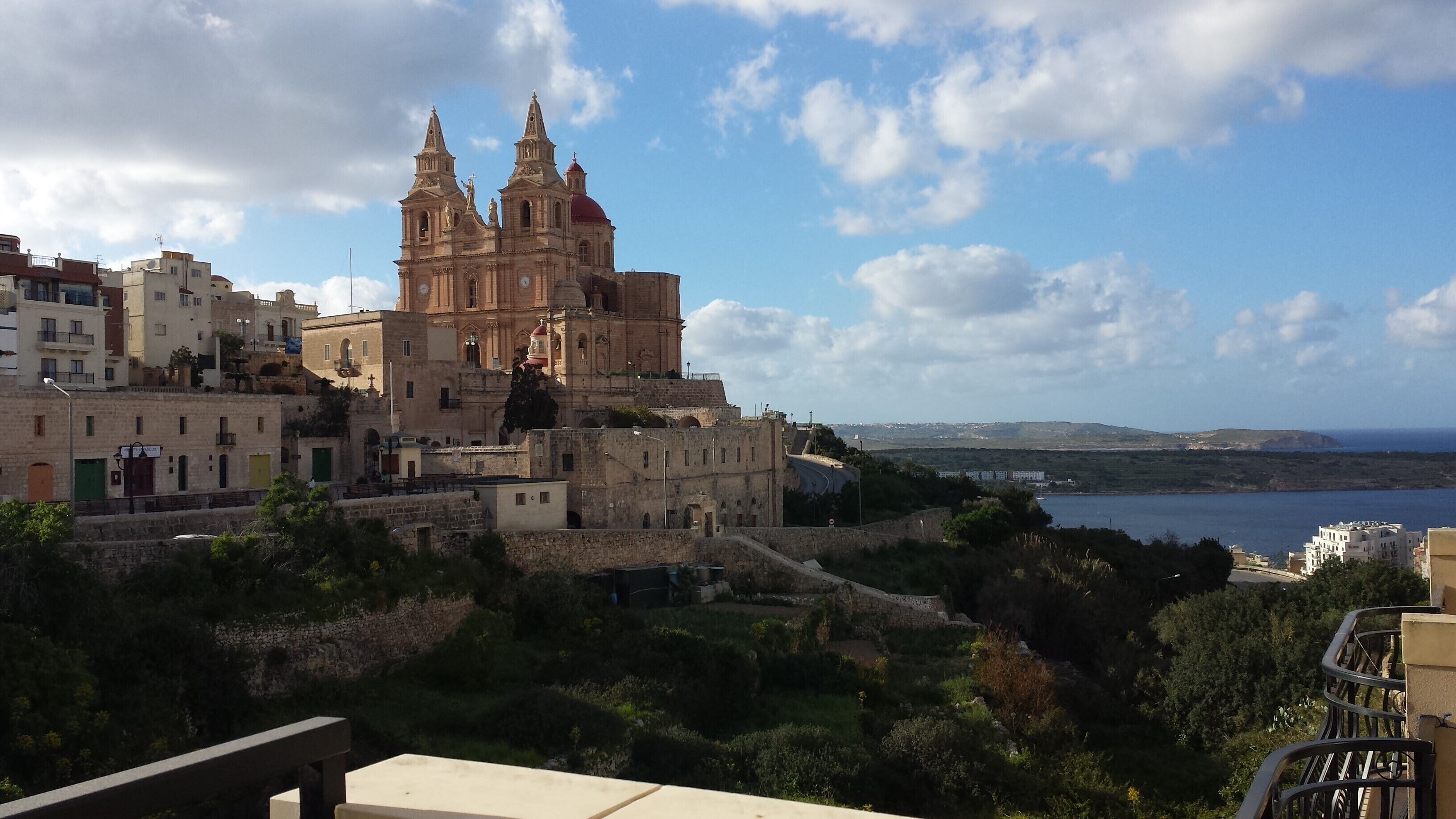 A historic church with twin towers, surrounded by residential buildings and a coastal view.