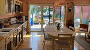 A kitchen with a central island, a dining area with a table and chairs, and a view through the glass doors to an outdoor patio.