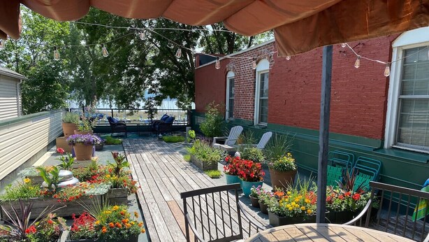 A wooden deck with potted plants and outdoor furniture, including chairs and a table.