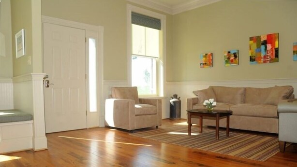 A living room with hardwood flooring, a beige sofa, a beige armchair, a coffee table, and a window with a view. - Renovated Train Station on Thoroughbred Horse Farm (Paris)
