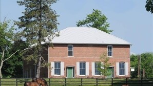 A brick building with a white roof and a fenced area with horses grazing. - Renovated Train Station on Thoroughbred Horse Farm (Paris)