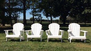 Four white Adirondack chairs arranged in a row on a grassy field with trees in the background. - Renovated Train Station on Thoroughbred Horse Farm (Paris)