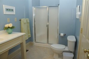 Une salle de bain équipée d’une douche, de toilettes, d’un lavabo et d’un vase avec des fleurs.
