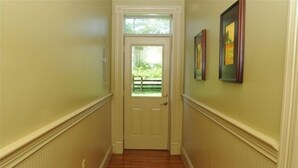 A narrow hallway with a wooden floor, a white door with a glass panel, and two framed pictures on the wall. - Renovated Train Station on Thoroughbred Horse Farm (Paris)
