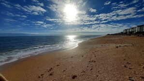 Una playa con huellas, cielo despejado y edificios al fondo.