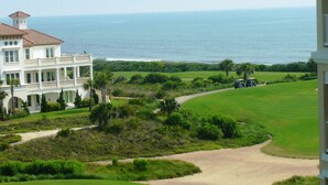 Un edificio grande de varios pisos con un balcón que da a un campo de golf y al océano.