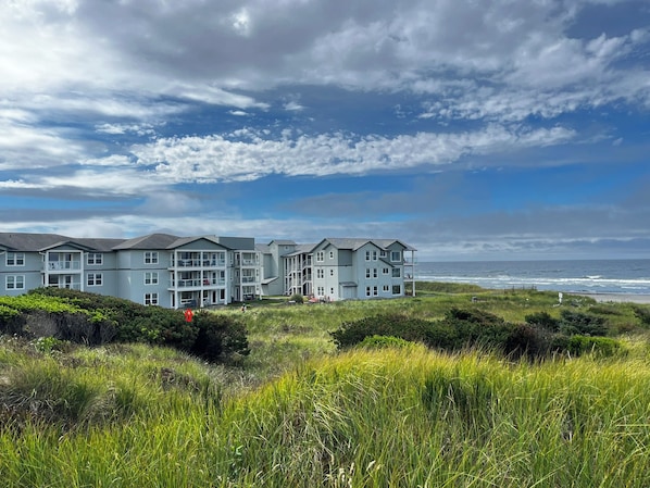 A coastal hotel with multiple floors and balconies, situated on a grassy hill overlooking the sea.