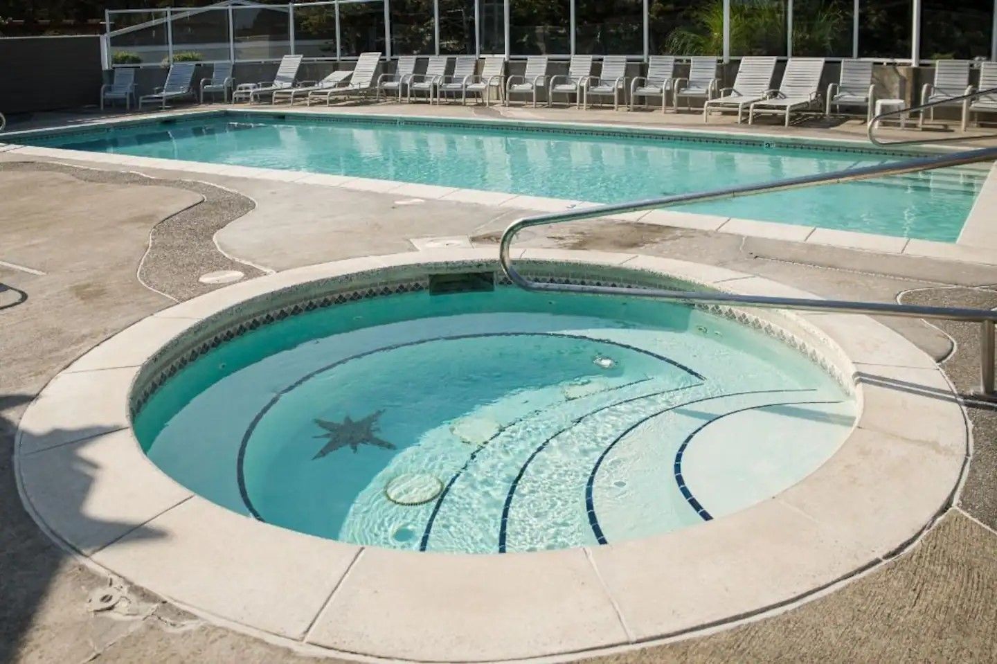 Un jacuzzi rond décoré d’une étoile de mer, entouré d’une piscine avec des chaises longues.