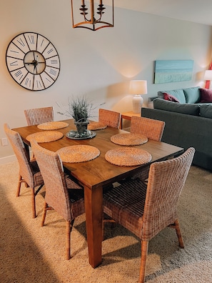 A dining area with a wooden table, wicker chairs, and a wall clock.