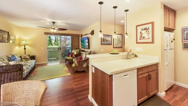 A modern kitchen with a central island, wooden cabinets, pendant lights, and a refrigerator. - Lovely Two Bedroom that Feels Like Home (Waikoloa)