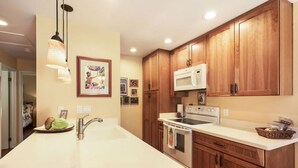 A kitchen with wooden cabinets, a white countertop, a sink, a stove, and a microwave. - Lovely Two Bedroom that Feels Like Home (Waikoloa)