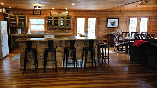 A cabin interior with a wooden interior, a kitchen area, and a dining space with bar stools. -  Log Home in the NATIONAL FOREST.  ATV/SNOWMOBILE TRAIL CROSS OUR PROPERTY (Hayward)