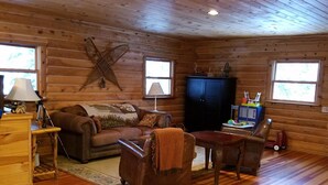 A cozy log cabin interior with a wooden floor, a leather sofa, a small table, and a television. -  Log Home in the NATIONAL FOREST.  ATV/SNOWMOBILE TRAIL CROSS OUR PROPERTY (Hayward)