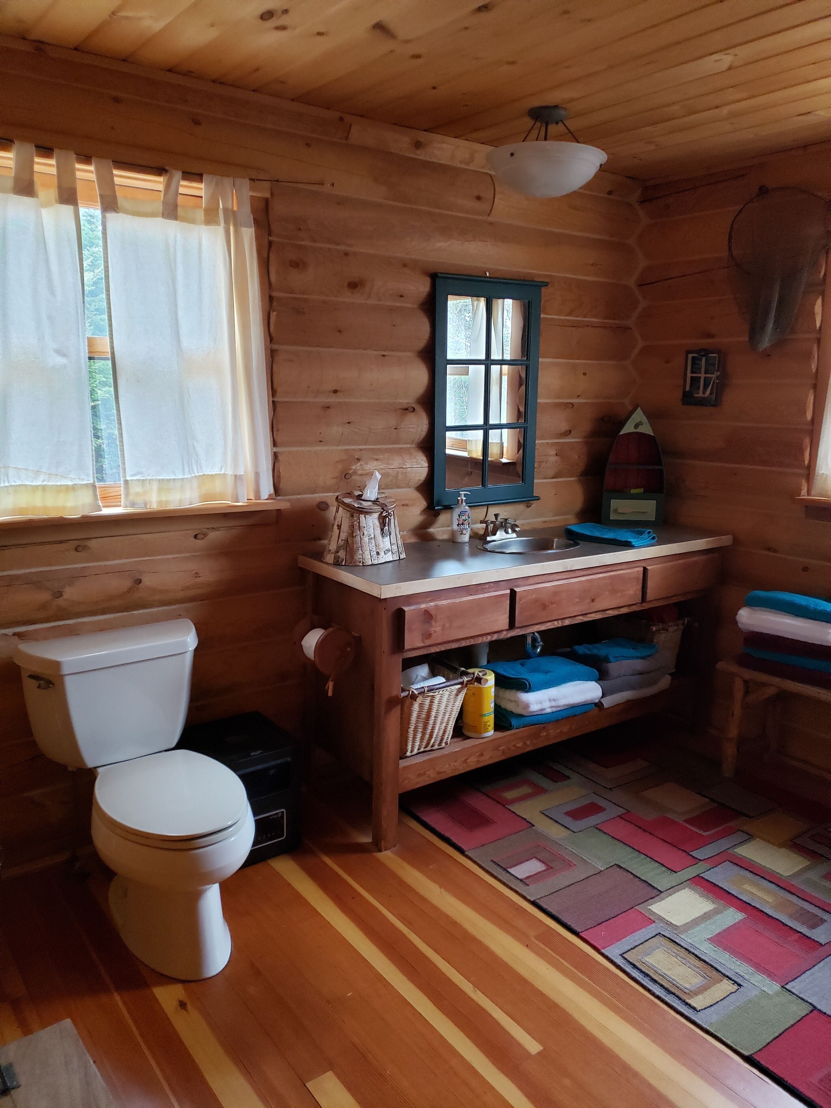 Ein Badezimmer einer Holzhütte mit Toilette, Waschbecken und Fenster.