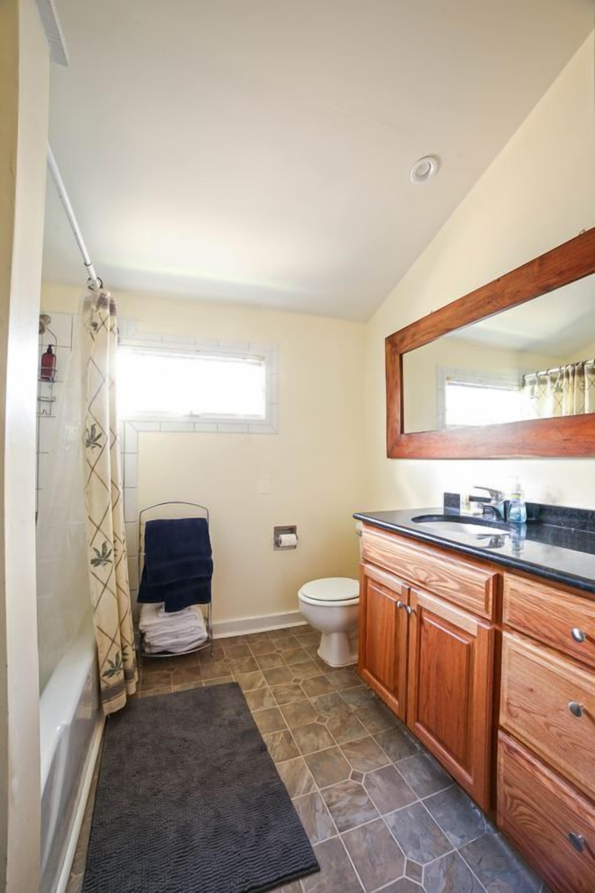 A bathroom with a shower, toilet, and wooden vanity with a mirror.