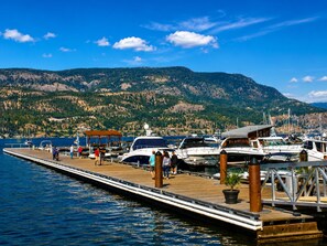 A dock with boats, a wooden pier, and a mountainous backdrop. - The Skye at Waterscapes Kelowna Luxurious Lake View Condo (Kelowna)