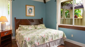 Een slaapkamer met een bed, een nachtkastje, een raam met uitzicht op groen en een ingelijste foto aan de muur.