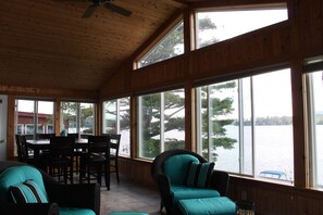 A wooden-paneled room with a dining table and chairs, large windows overlooking a body of water. - Beautiful Waterfront home with deep water dock on Onota Lake. Huge covered deck. (Pittsfield)
