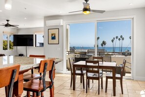 A modern kitchen with a large island, dining area, and a balcony with a view of the ocean.