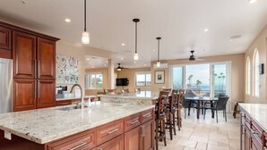 A spacious kitchen with a large island, wooden cabinets, and a dining area with a view. - Luxurious Sea Crest Oceanview Villa- by Main Beach (Santa Cruz)