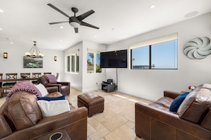 A spacious living room with leather sofas, a ceiling fan, a flat-screen TV, and a dining area with a table and chairs.