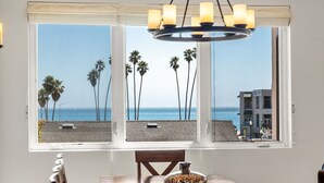 A dining area with a view of the beach and palm trees through large windows. - Luxurious Sea Crest Oceanview Villa- by Main Beach (Santa Cruz)