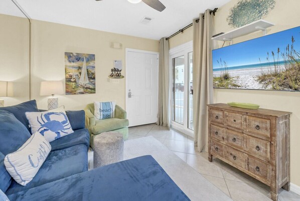 A living room with a sofa, a wooden dresser, a painting of a beach, and a door leading to a balcony. - Endless Summer - Steps to Beach, 2BR 2BA newly remodeled bathrooms (Santa Rosa Beach)