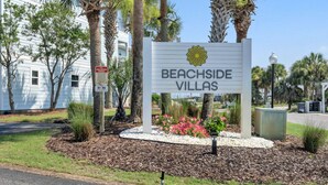 Skilt for Beachside Villas med palmetræ og blomsterbed foran.