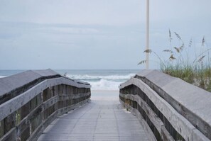 En støbt træpromenade der fører til stranden med udsigt over havet.