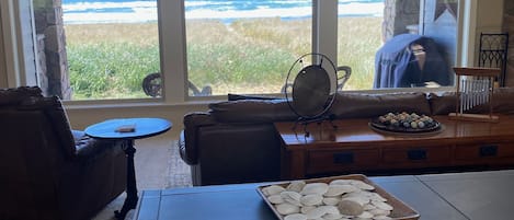 Une pièce dotée d’une grande fenêtre donnant sur l’océan, d’un mur en pierre, d’un canapé en cuir, d’une petite table ronde et d’un plateau rempli de coquillages.