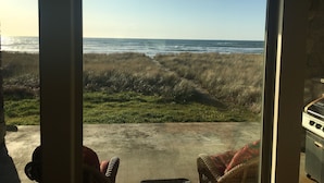 A view from a room with a large window overlooking the ocean, a concrete floor, and a wicker chair. - Beach Star - Classic, Elegant & Comfortable Beachfront Home! (Rockaway Beach)